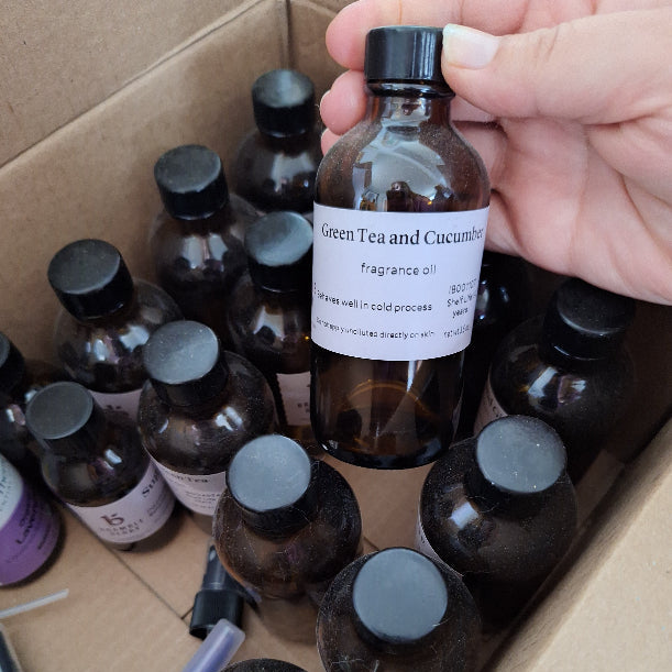 Hand holding a bottle of 'Green Tea and Cucumber' fragrance oil with other bottles in the background.