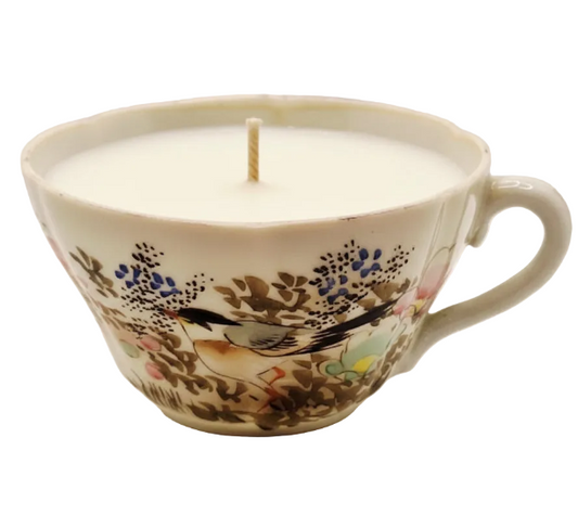 Candle in a decorative teacup with floral and bird design on a white background