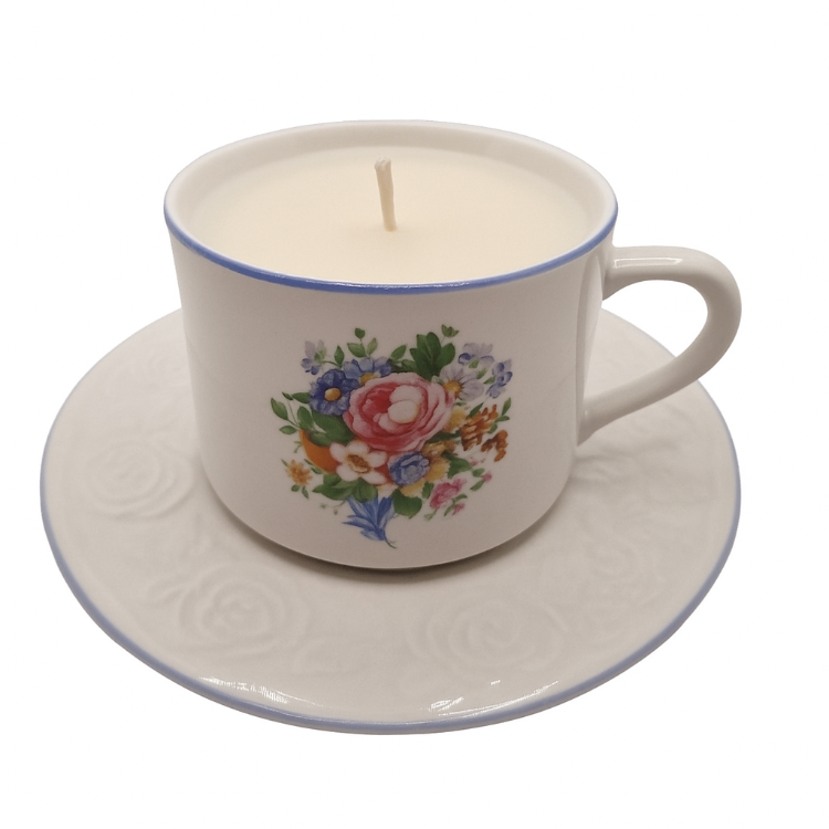 Ceramic teacup and saucer with a floral design containing a lit candle on a white background