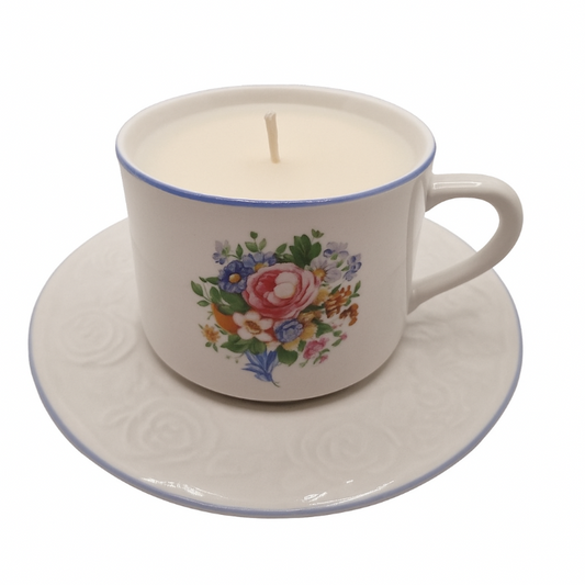 Ceramic teacup and saucer with a floral design containing a lit candle on a white background