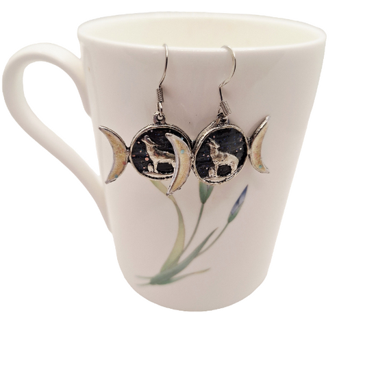 Pair of earrings with wolf and moon design on a mug with floral pattern