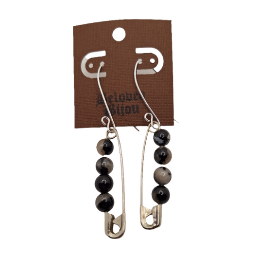 Pair of earrings with safety pins and black beads on a brown card with brand name.