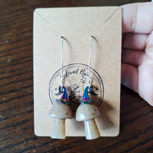 Pair of mushroom-shaped earrings on a branded card held by a hand.