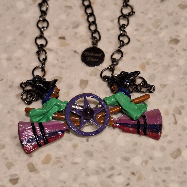 Colorful witch-themed necklace with broomstick and hat on a textured surface