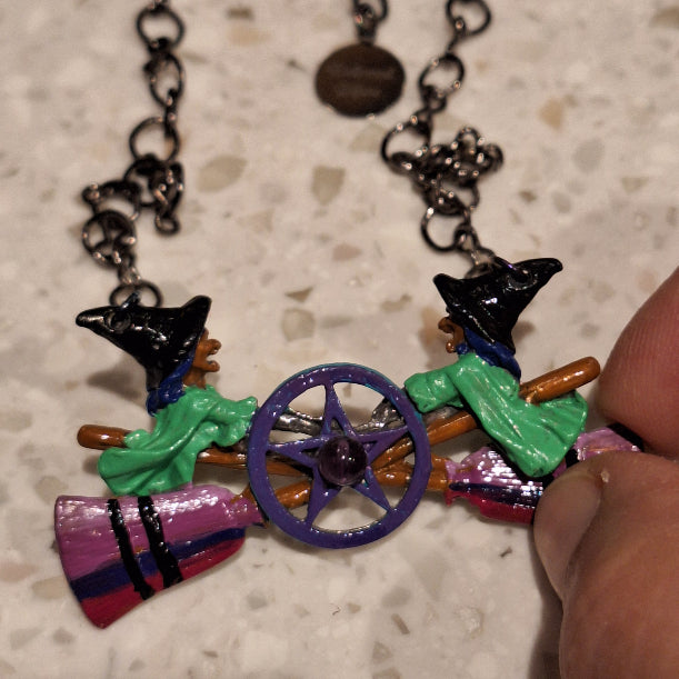 Colorful witch and broom charm on a chain against a textured surface