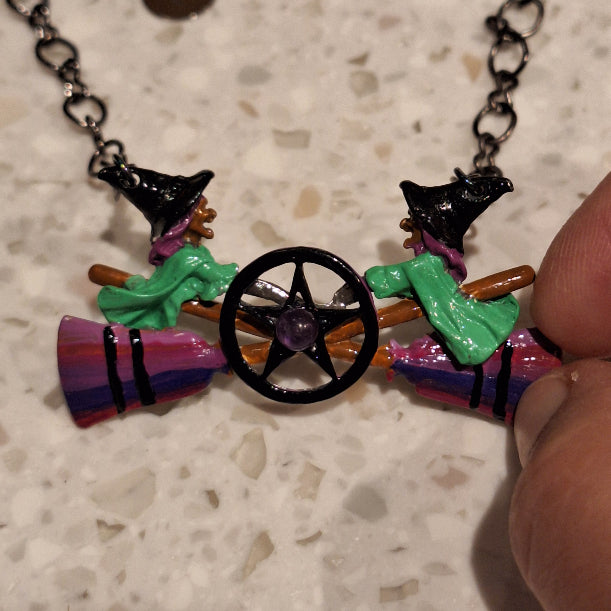 Colorful witch-themed necklace with broomstick and hat on a textured surface