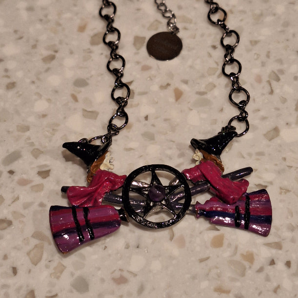 Colorful witch hat and broom charm on a chain against a textured beige background