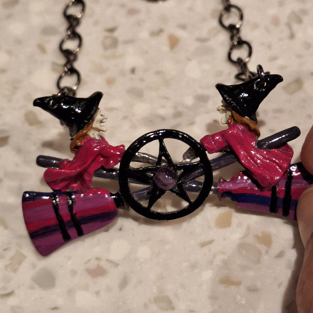 Colorful witch-themed necklace with a broomstick, hat, and cauldron on a textured surface.