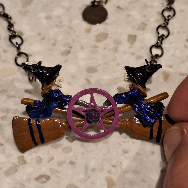 Close-up of a necklace with witch-themed necklace on a textured surface