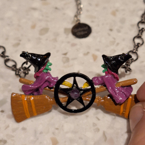 Colorful witch necklace with broom and cats on a textured surface