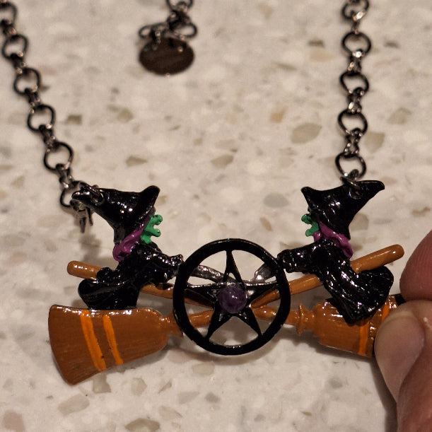 Halloween-themed necklace with witch hat, broomstick, and cauldron charms on a chain.