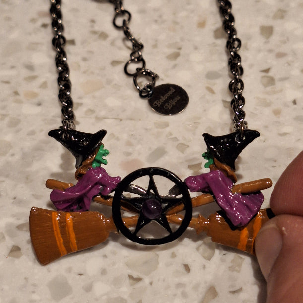 Colorful witch-themed necklace with broomstick, hat, and cauldron charms on a chain.