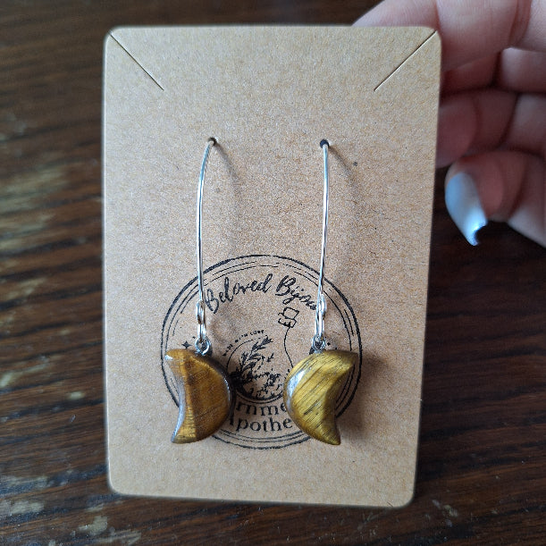 crescent moon shaped earrings on a branded card with a wooden surface background