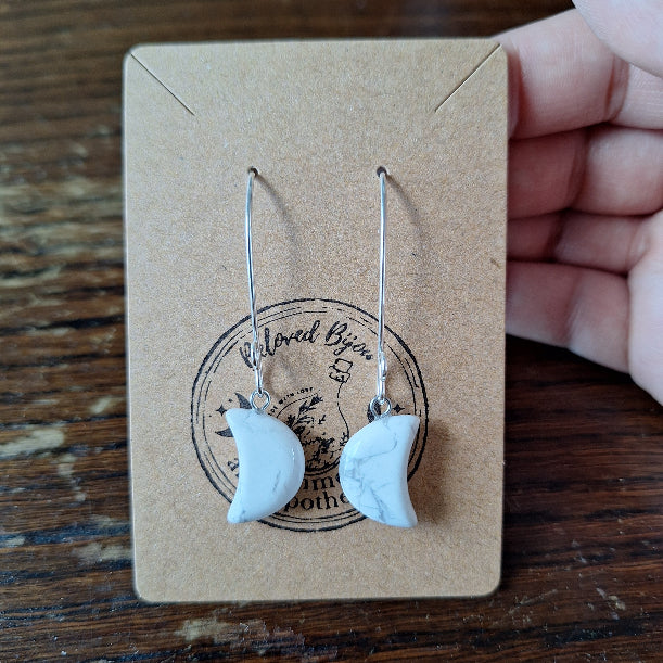 crescent moon earrings on a branded card with a wooden surface background