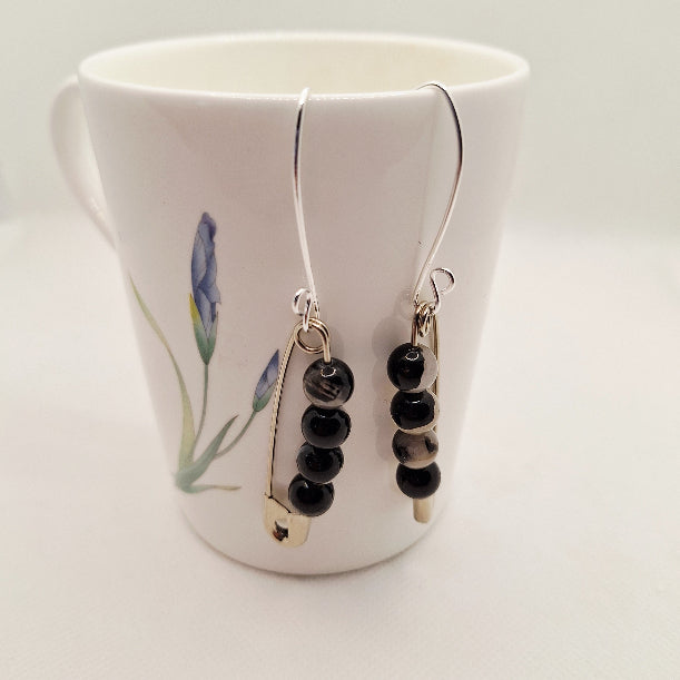 Black beaded earrings hanging from a white mug with floral design