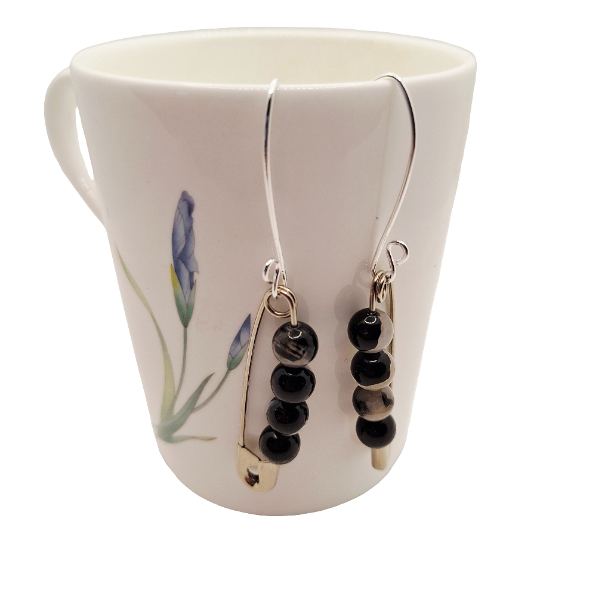 Black beaded earrings hanging from a white mug with floral design