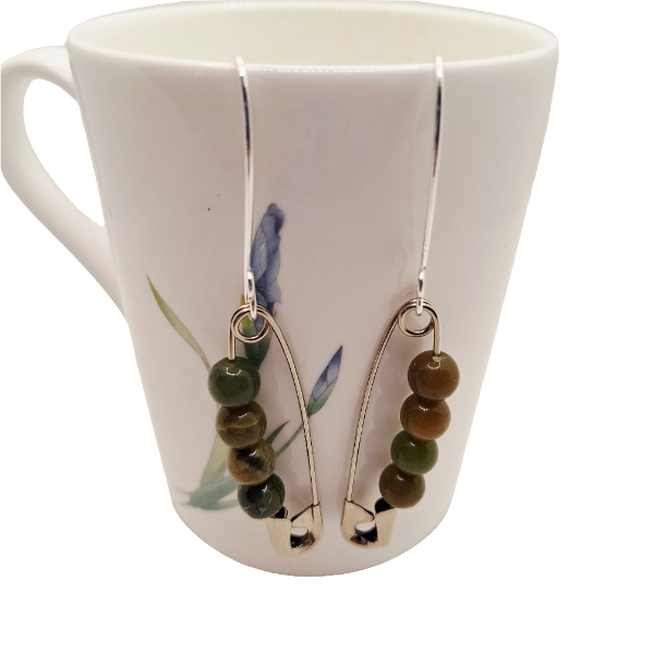 Pair of earrings with green beads hanging from a mug with floral design