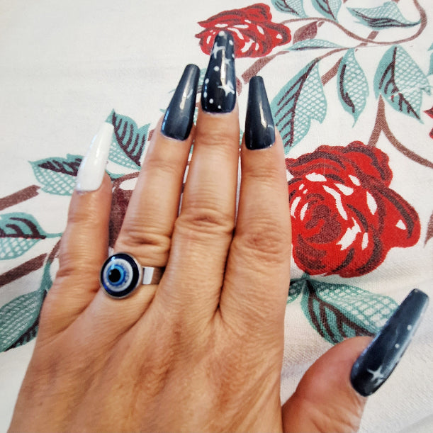 Hand with black nail polish and a blue ring on a floral background