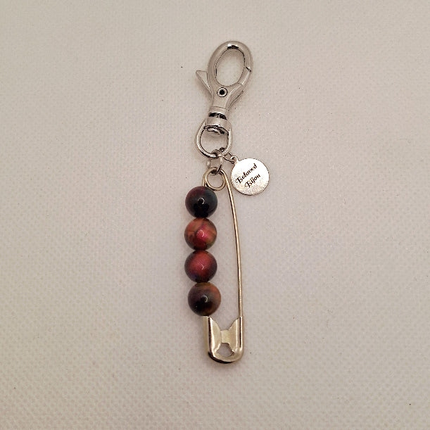 Keychain with safety pin and tiger's eye beads on a beige background