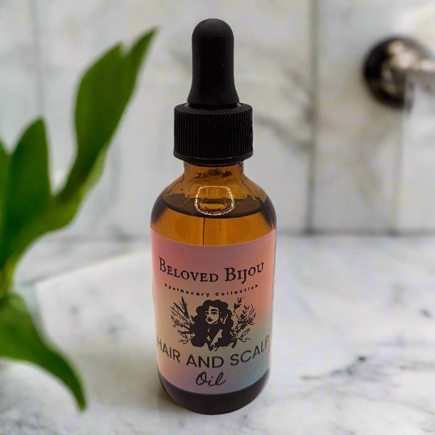 Bottle of Beloved Bijou hair and scalp oil on a marble surface with a plant in the background.