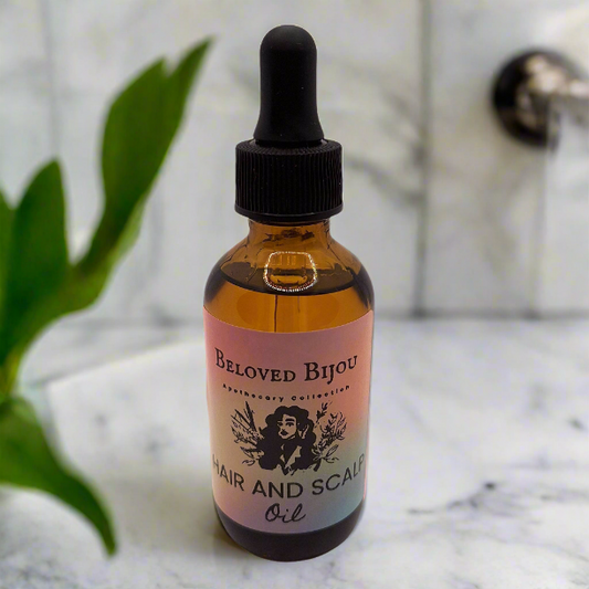 Bottle of Beloved Bijou hair and scalp oil on a marble surface with a plant in the background.
