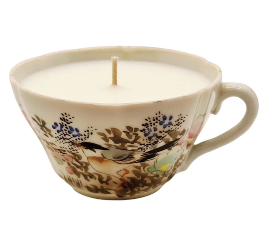 Candle in a decorative teacup with floral and bird design on a white background