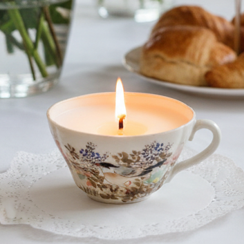 Candle in a decorative teacup with a plate of pastries in the background