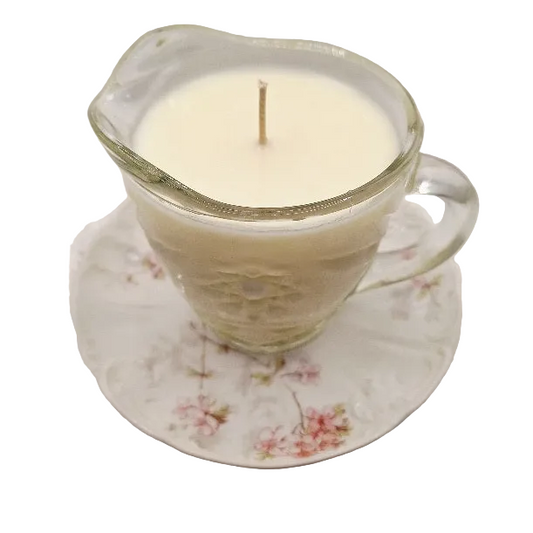 Candle in a glass creamer cup with floral saucer on a white background