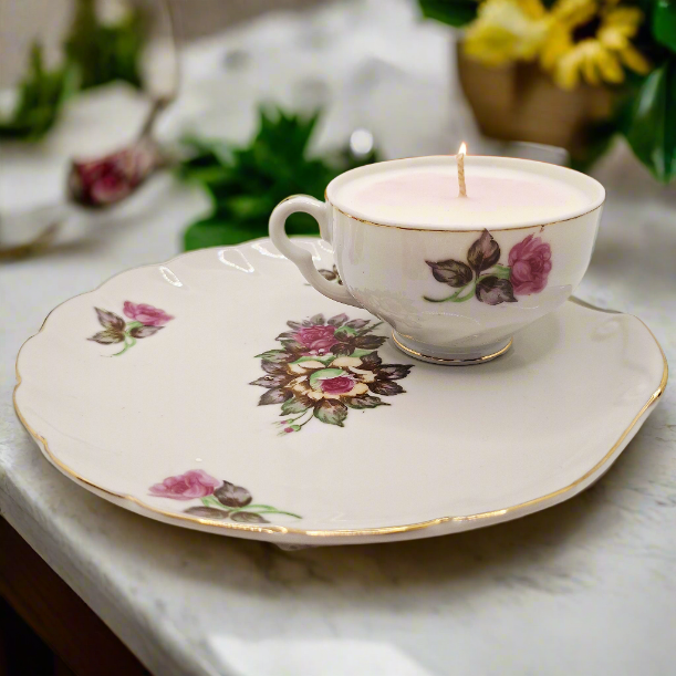 Teacup candle and saucer with floral design, containing a lit candle on a marble surface.