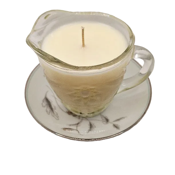 Candle in a glass creamer cup with a decorative base on a white background