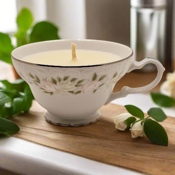 Teacup candle with floral design on a wooden surface with greenery