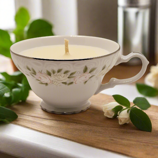 Teacup candle with floral design on a wooden surface with greenery