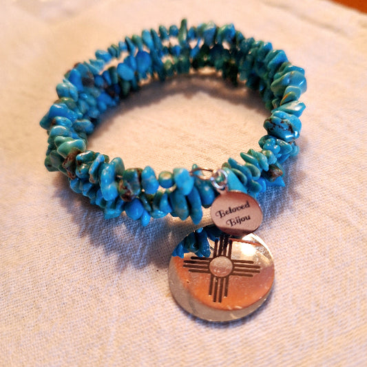 Turquoise beaded bracelet with a copper charm on a beige fabric background