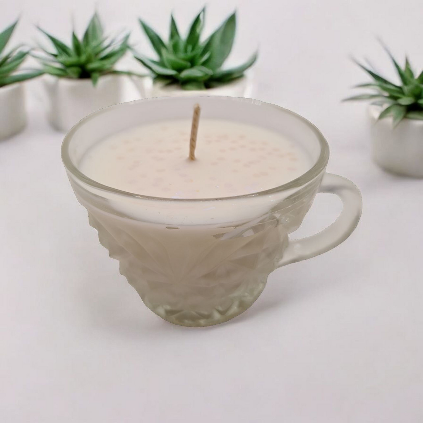 Candle in a glass mug with plants in the background