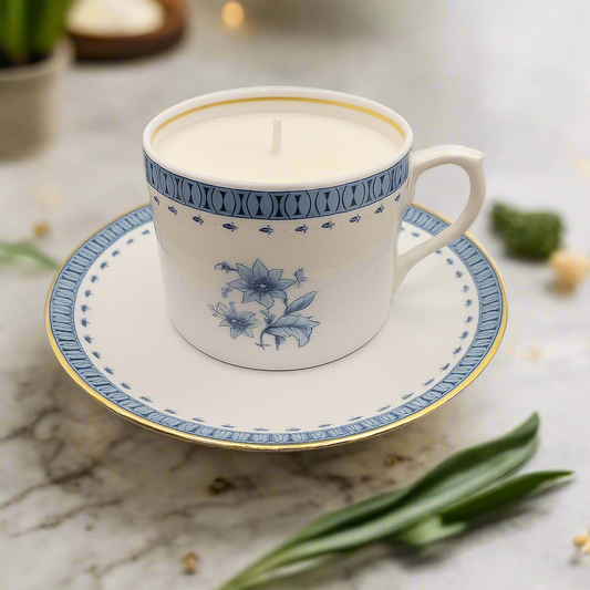 Candle in a decorative teacup on a saucer with floral patterns, placed on a marble surface.