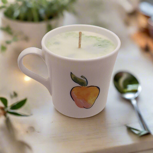 Candle in a white mug with an apple design on a wooden surface.