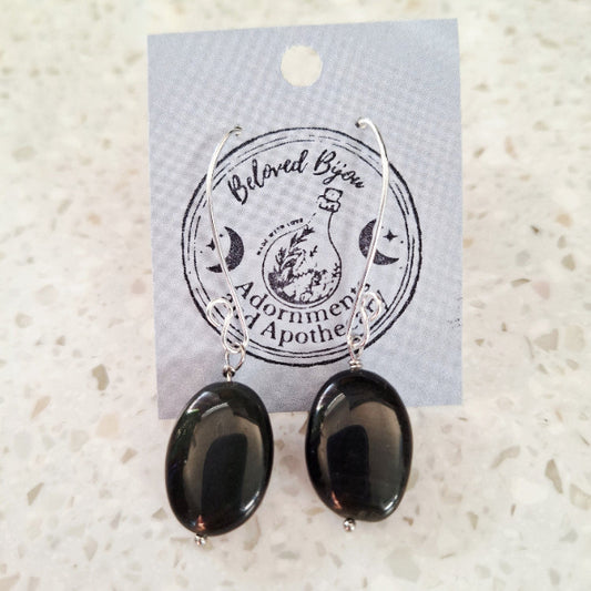 Black oval obsidian earrings on a branded card with a textured white background