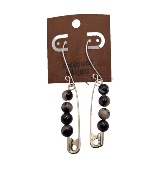 Pair of earrings with safety pins and black beads on a brown card with brand name.