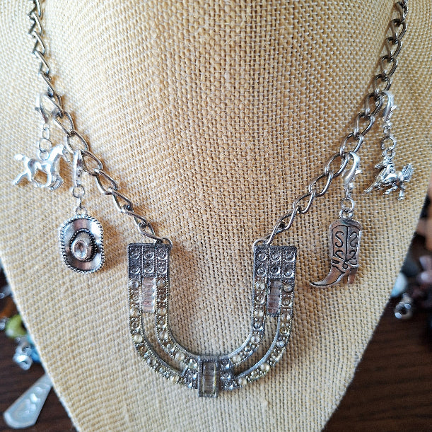 Silver necklace with horse, boot, and horseshoe charms on a beige fabric background