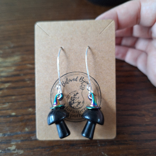 Pair of mushroom earrings on a branded card with a wooden surface underneath