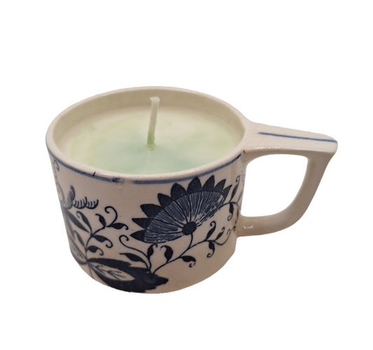 Ceramic espresso cup with floral design containing a candle on a white background