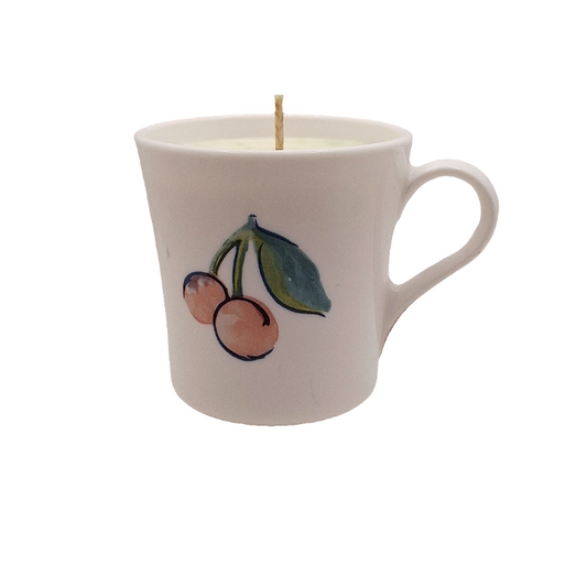 White mug with cherry design containing a candle on a white background