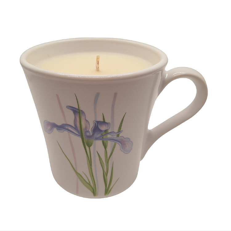 milk glass mug with a floral design containing a lit candle on a white background