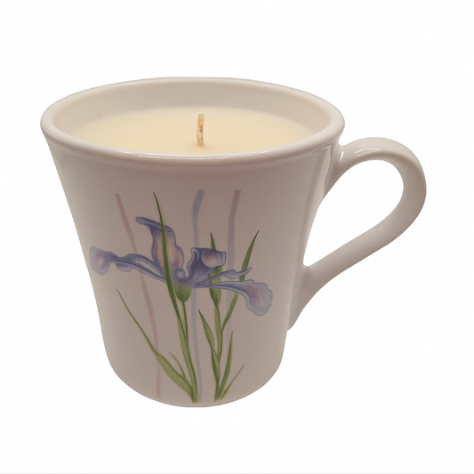 milk glass mug with a floral design containing a lit candle on a white background