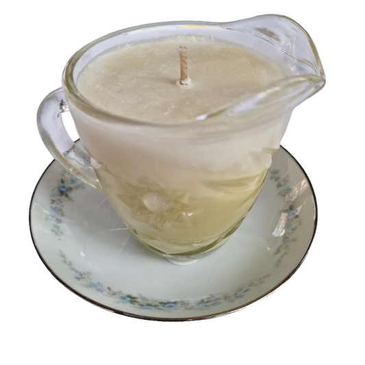 Candle in a glass creamer cup with handle on a floral saucer