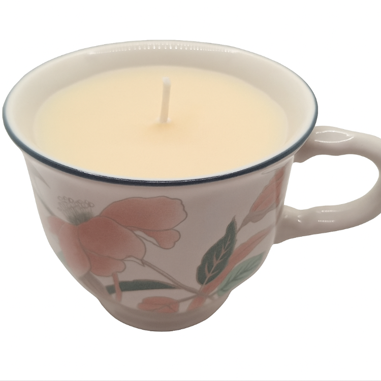 Candle in a decorative teacup with floral patterns on a white background
